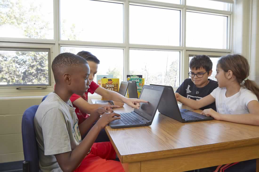 This is an image of students working on a laptop together one is poitning at the screen
